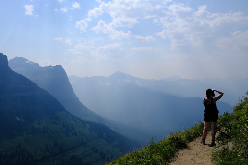 a woman standing on a trail looking at the mountains