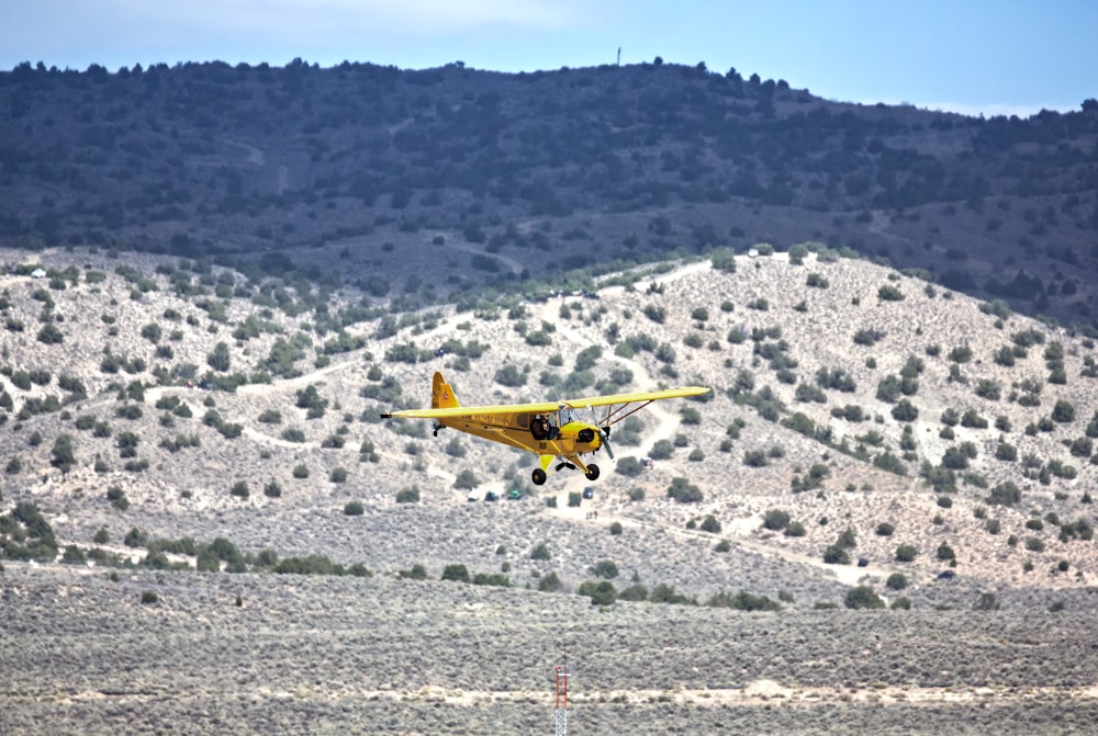 a small yellow airplane flying over a mountain