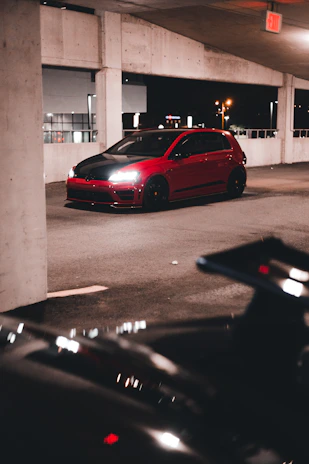 A sleek black car parked inside a modern, industrial-style garage with crimson accents.