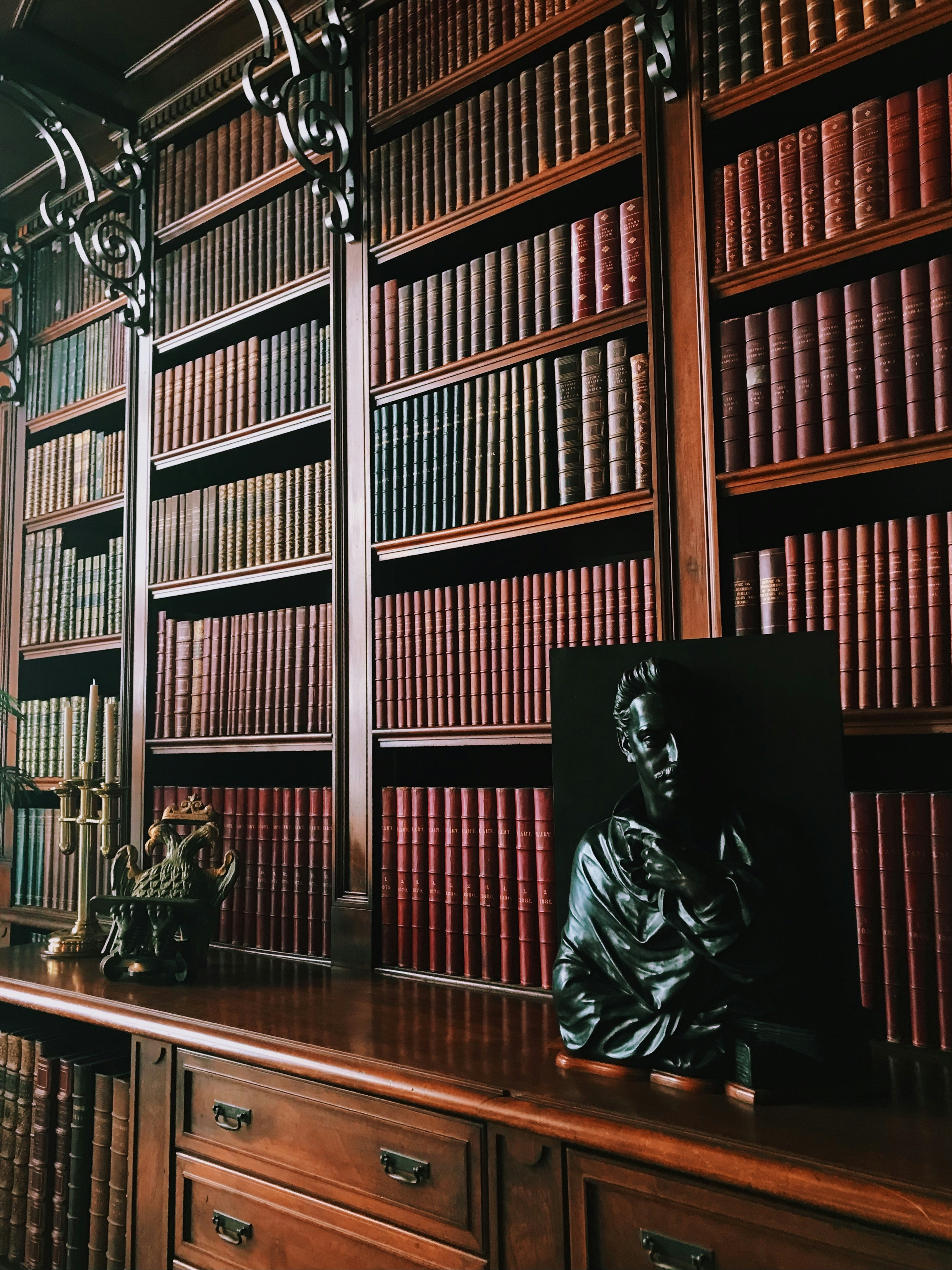 a statue of a man sitting on a desk in front of a bookshelf