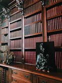 a statue of a man sitting on a desk in front of a bookshelf