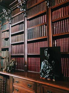 a statue of a man sitting on a desk in front of a bookshelf