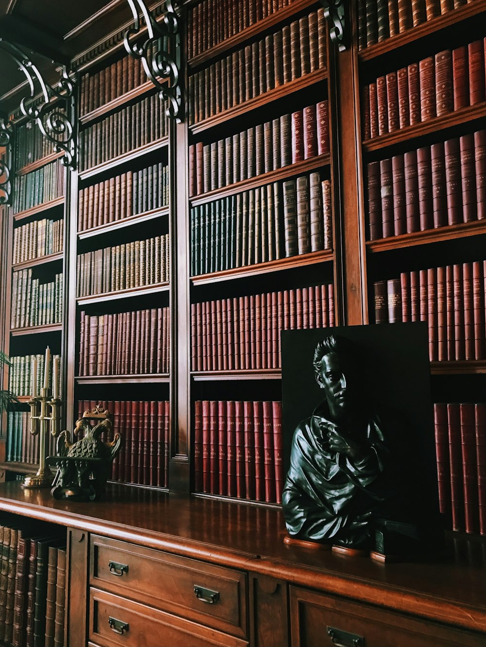 a statue of a man sitting on a desk in front of a bookshelf
