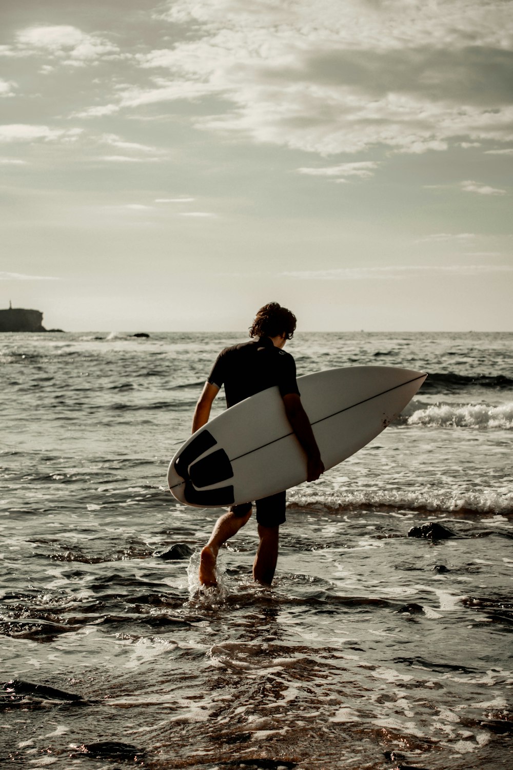 a man walking into the ocean with a surfboard