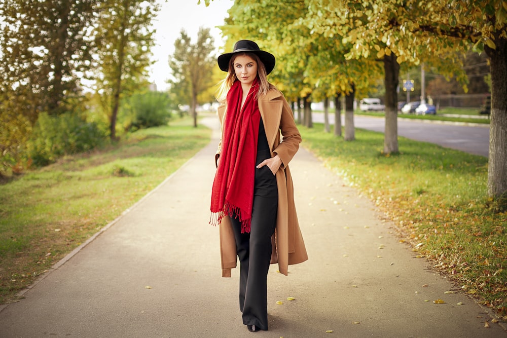 a woman in a hat and coat is walking down a path