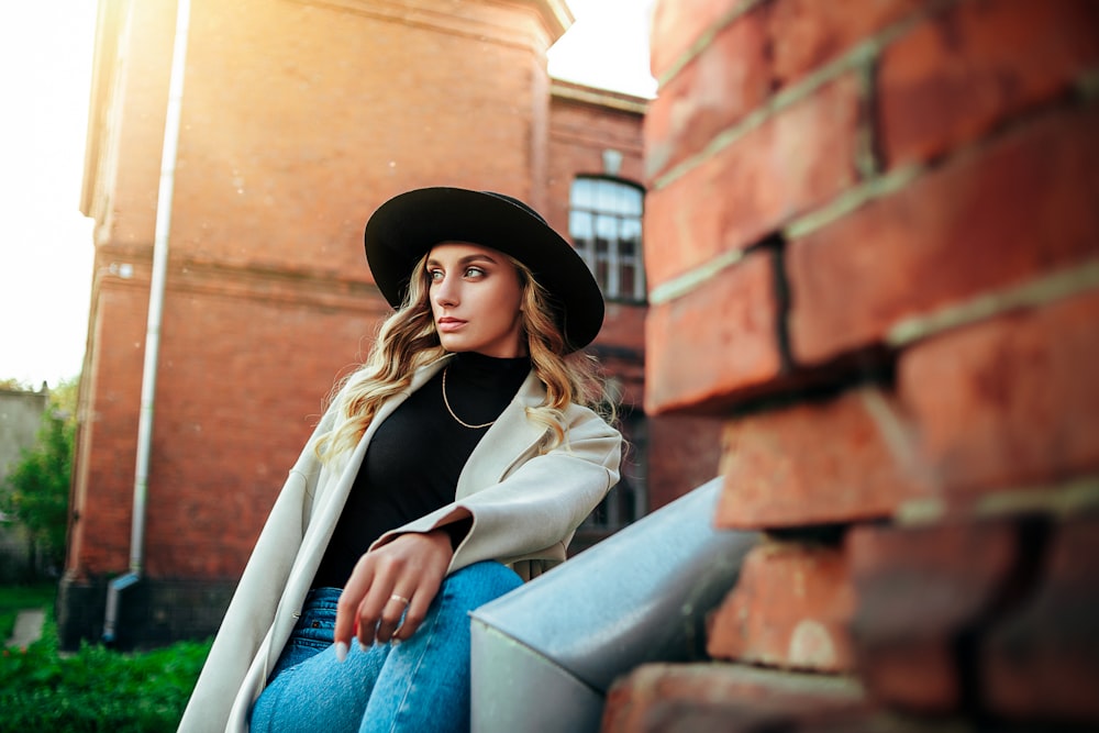 a woman wearing a black hat sitting on a brick wall