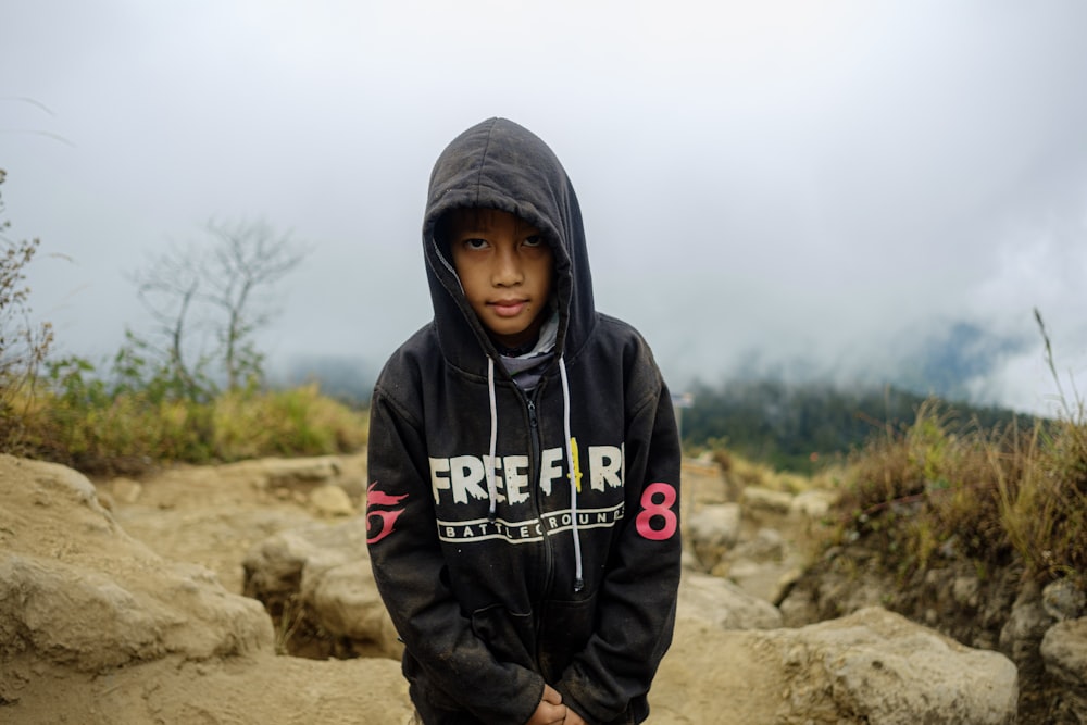 a young boy in a black hoodie standing on a rocky hillside