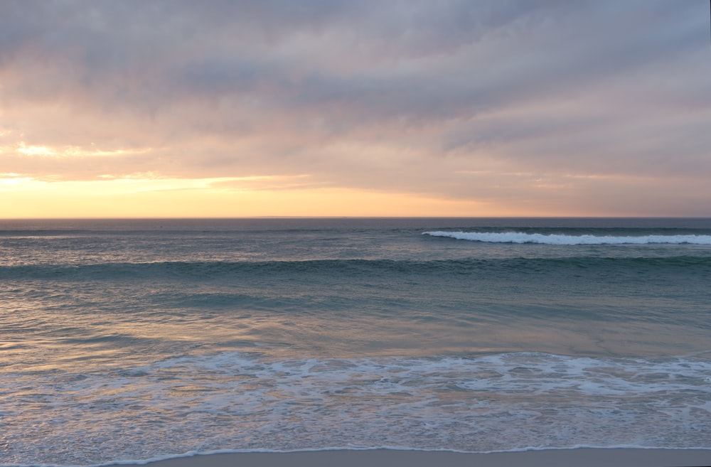 the sun is setting over the ocean with a wave coming in