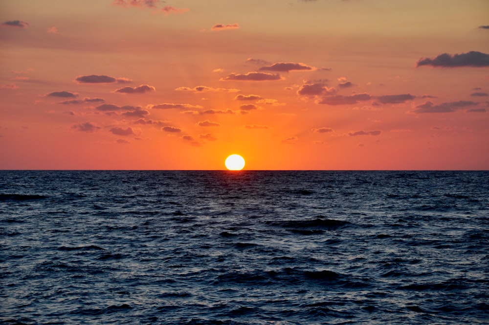 the sun is setting over the ocean on a cloudy day