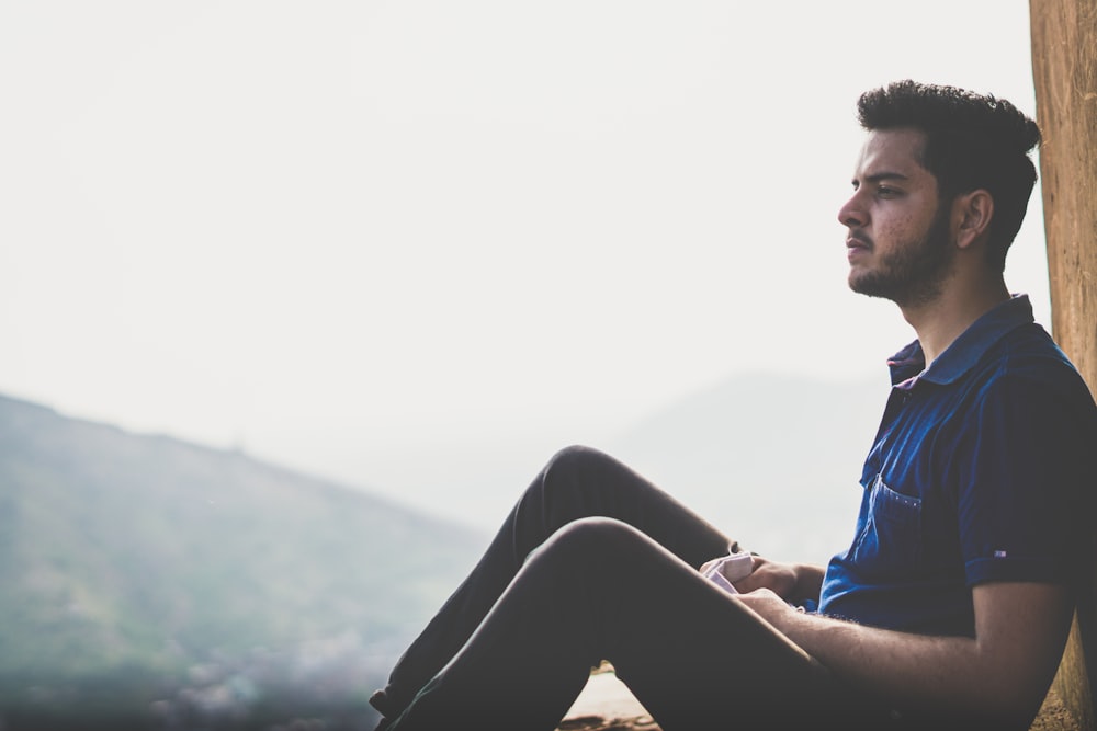 a man sitting on a ledge with a mountain in the background