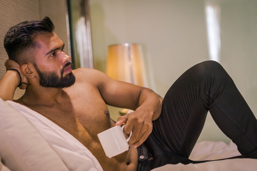 Un uomo a torso nudo che si trova su un letto che tiene un telefono cellulare