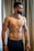 a man without a shirt standing in front of a window