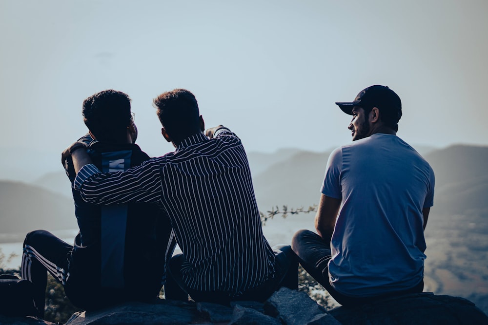 a couple of men sitting on top of a rock