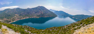 A panoramic view of Nainital's tranquil lake surrounded by green hills under a clear blue sky.