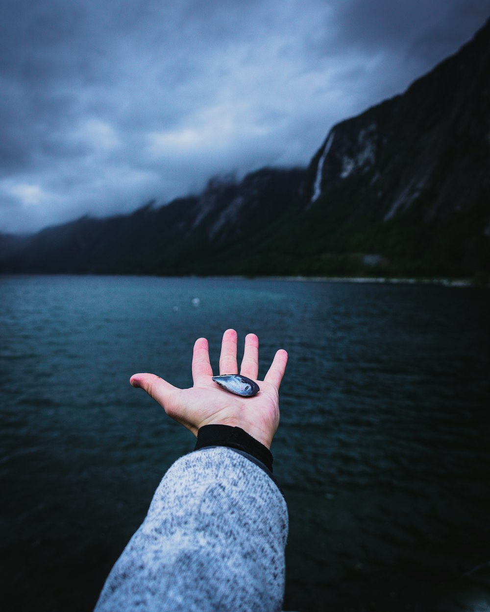 a person holding their hand out towards a body of water