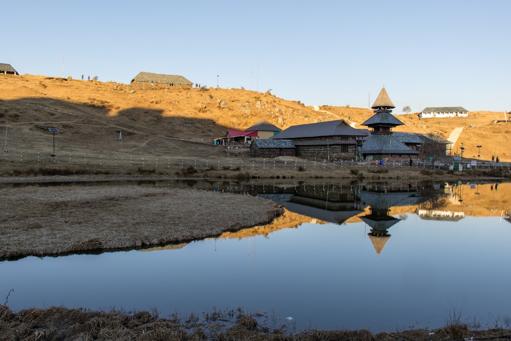 a small lake in front of a hill with a house on top of it