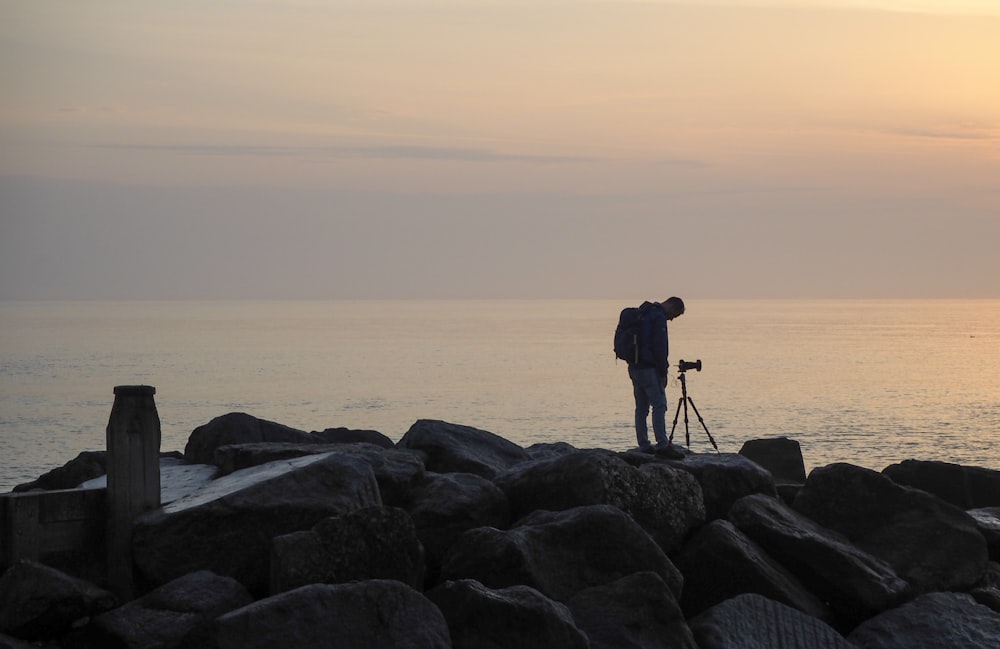 a man standing on top of a rocky beach next to the ocean