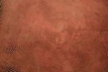 A series of concentric wavy lines form a hypnotic pattern, creating an optical illusion effect. The lines vary in thickness and spacing, converging towards a central point and generating a sense of movement and depth.