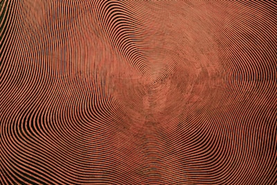 A series of concentric wavy lines form a hypnotic pattern, creating an optical illusion effect. The lines vary in thickness and spacing, converging towards a central point and generating a sense of movement and depth.