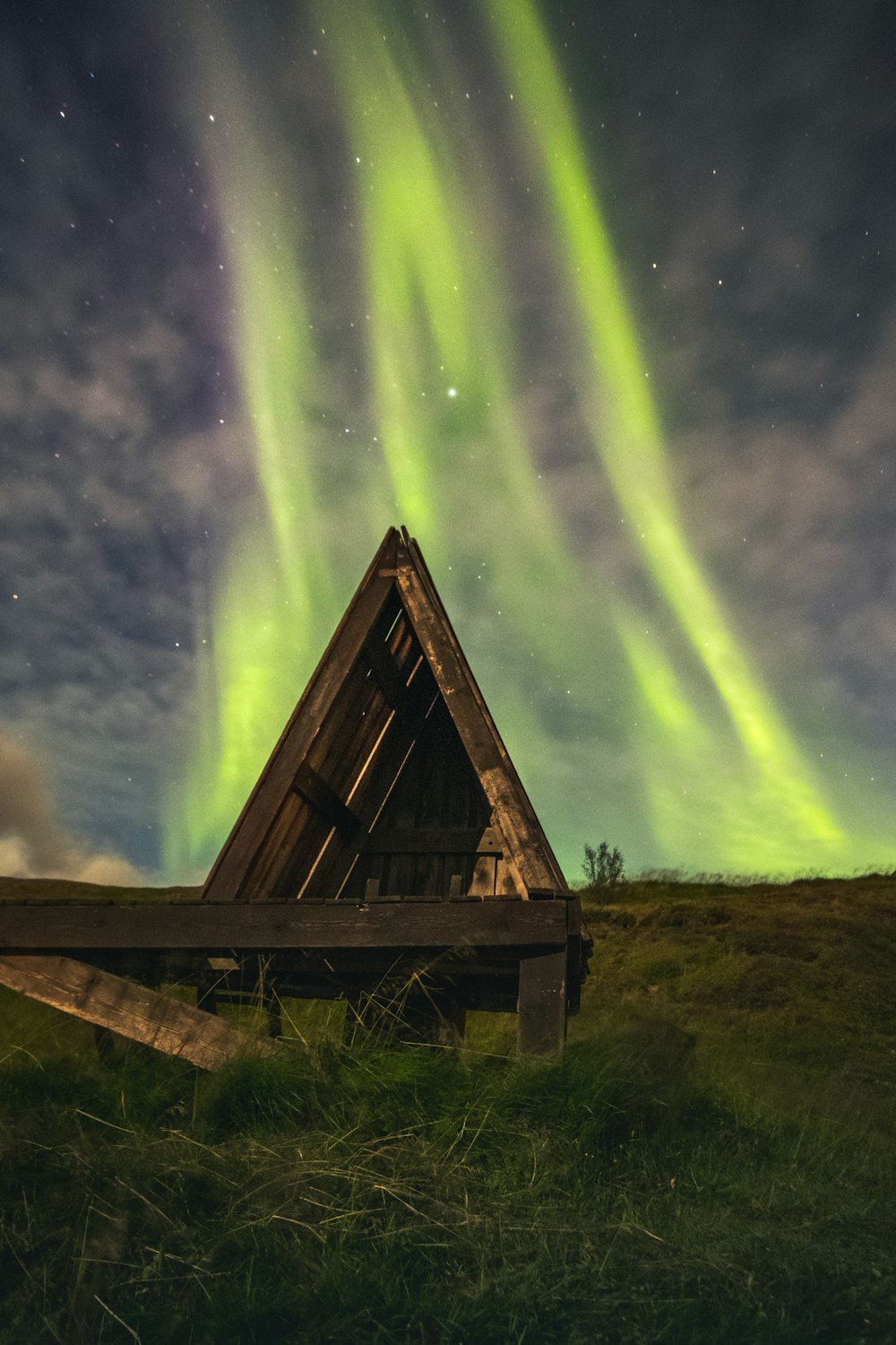 a wooden structure in a grassy field under a green and purple sky