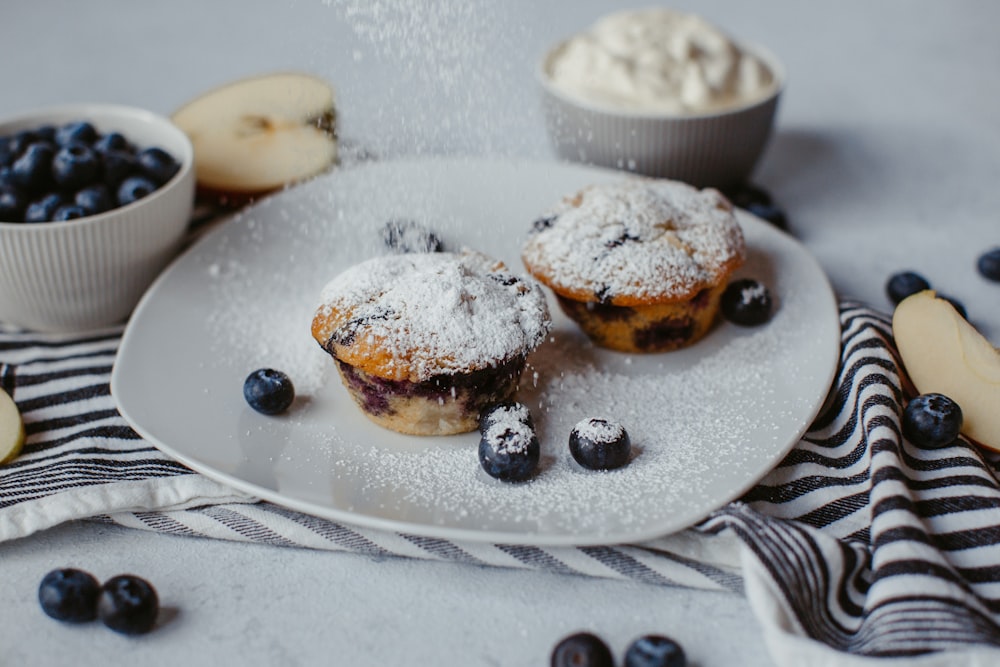 a white plate topped with blueberry muffins covered in powdered sugar