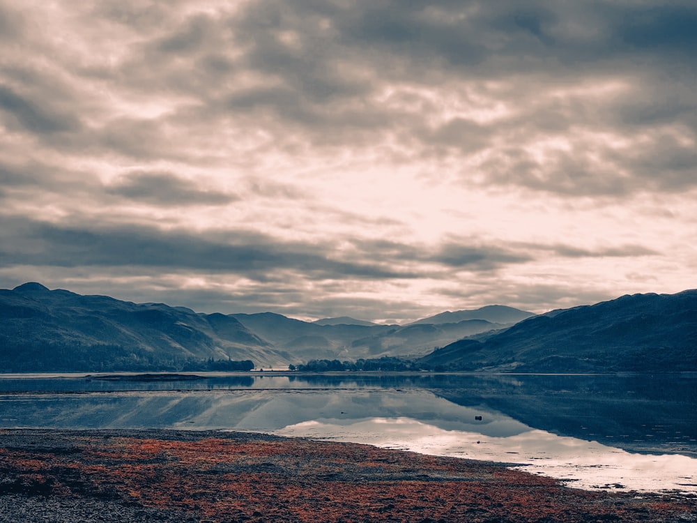 a body of water surrounded by mountains under a cloudy sky