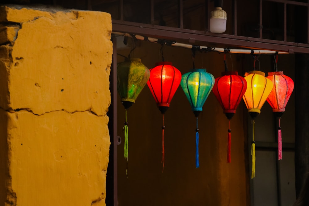 a row of colorful lanterns hanging from a yellow wall