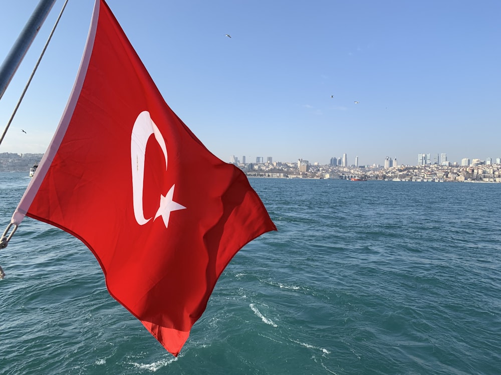 a flag on a boat in the water with a city in the background