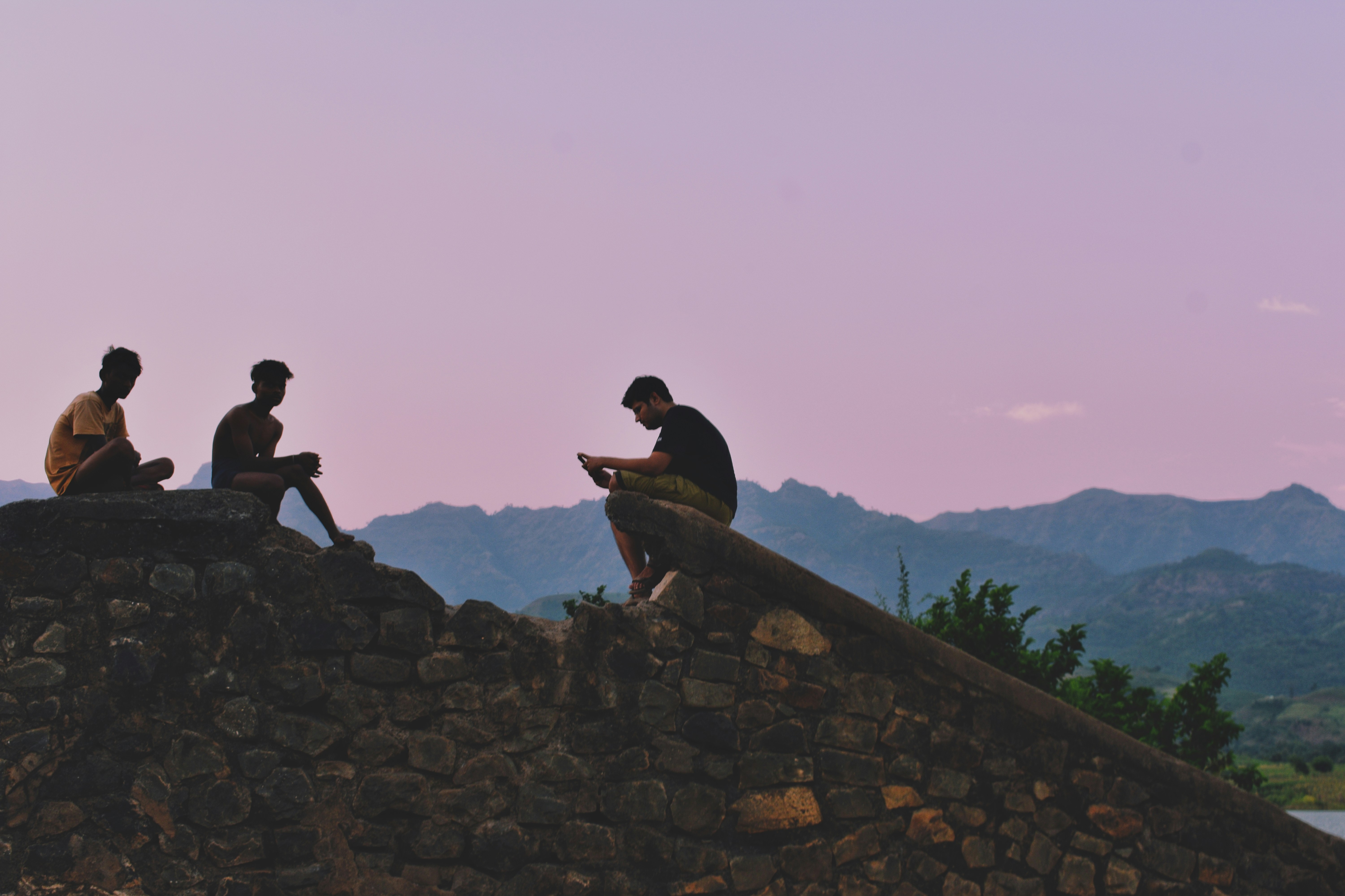 three men sitting on a stone wall looking at their cell phones