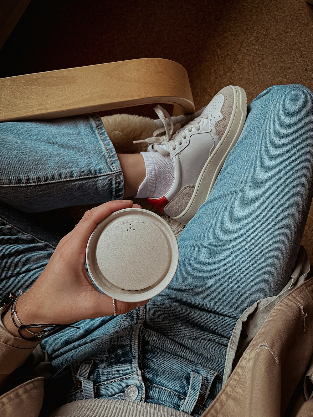 una persona seduta sul pavimento con in mano una tazza di caffè