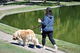 a woman walking a dog on a leash next to a lake