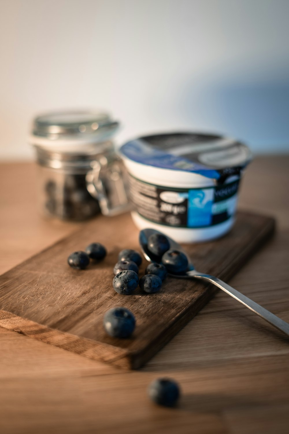 a wooden cutting board topped with blueberries next to a jar of yogurt