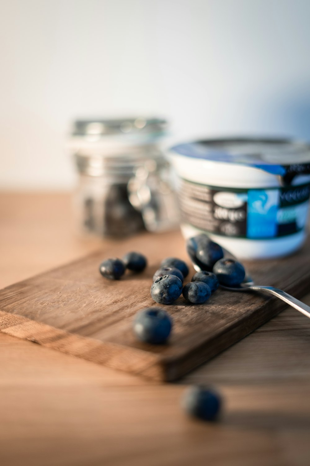 una tabla de cortar de madera cubierta con arándanos junto a un frasco de yogur