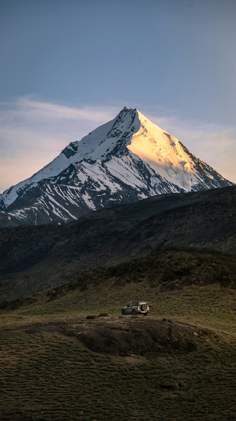 a snow covered mountain in the distance with a car parked in the foreground