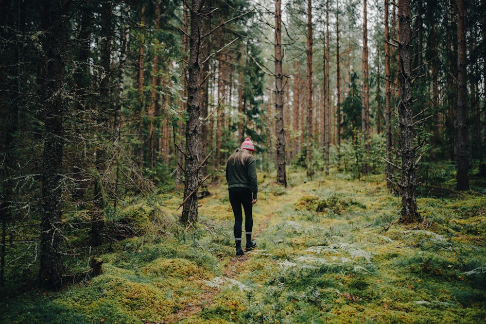 a woman walking through a forest with lots of trees