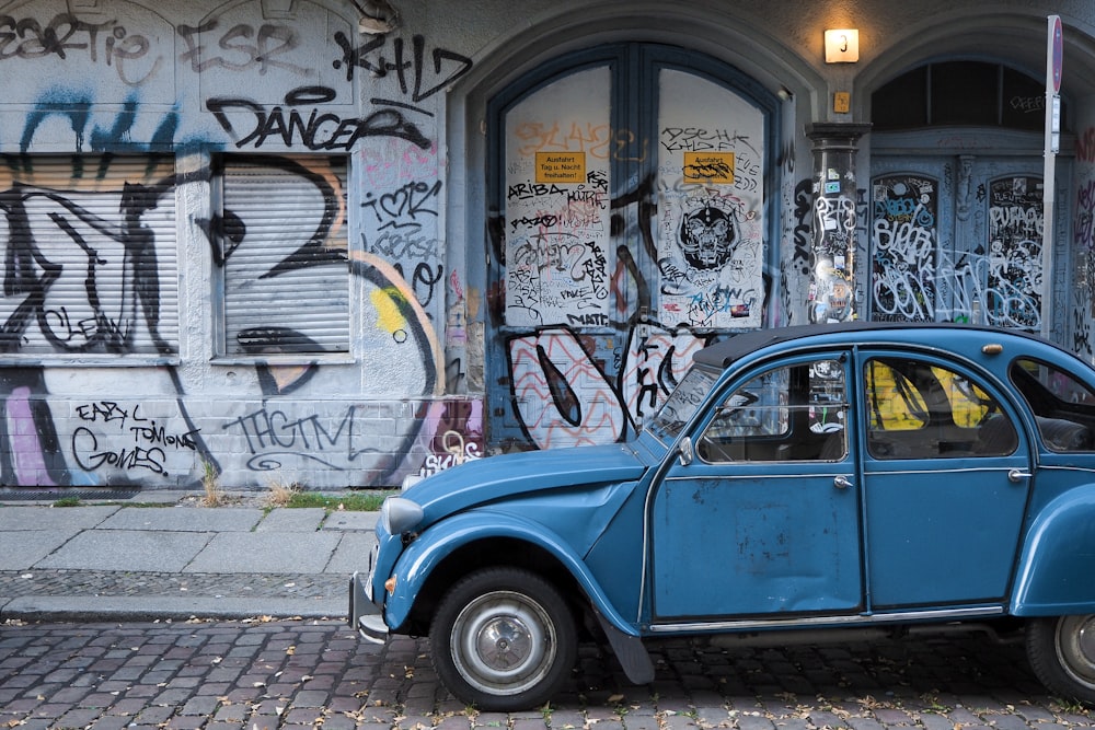 a blue car parked in front of a building covered in graffiti