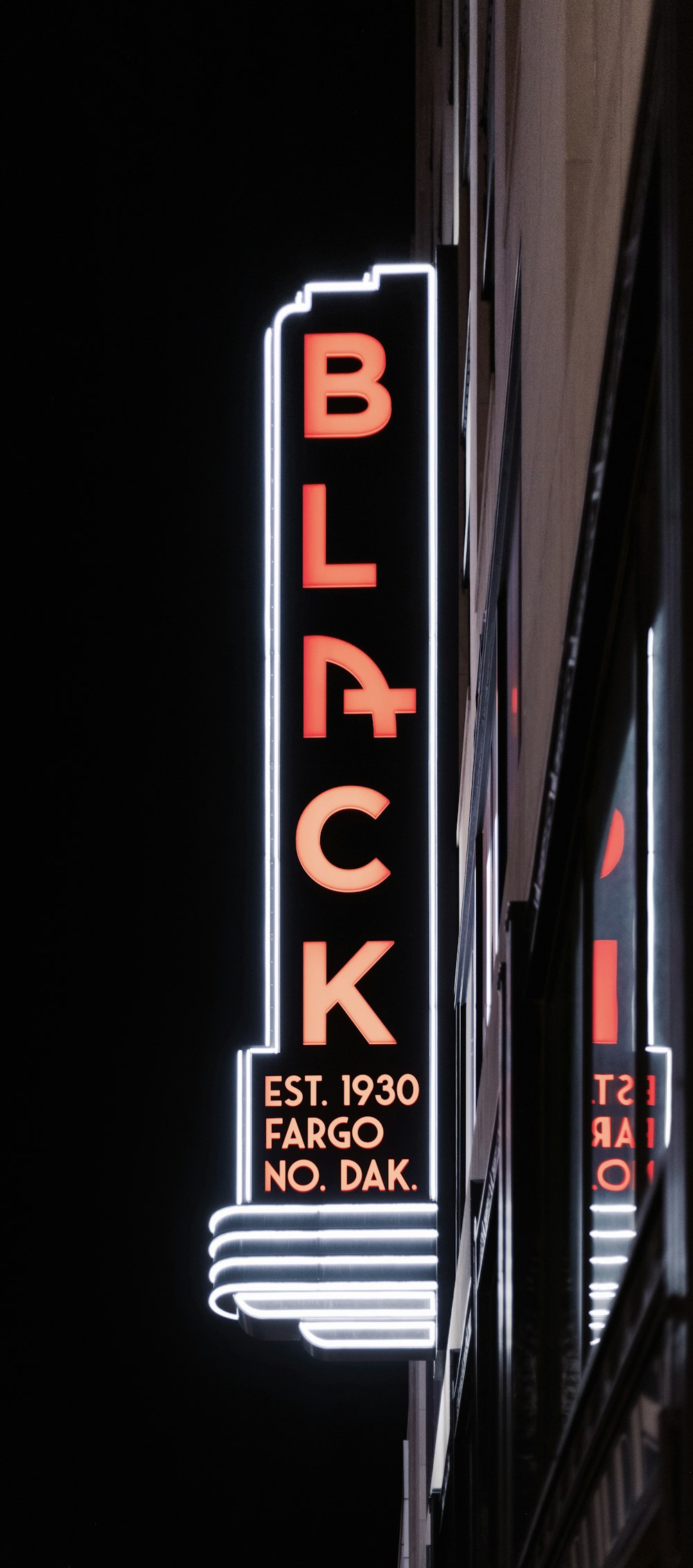 Un letrero negro está iluminado en el costado de un edificio