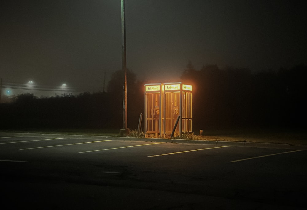 a small outhouse in a parking lot at night