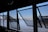 Several large open windows frame a view of a calm river with a distant shoreline. Through the windows, part of a boat with the name 'Porto Alegre' is visible. The sky is clear, and the water's surface reflects sunlight, creating a shimmering effect.