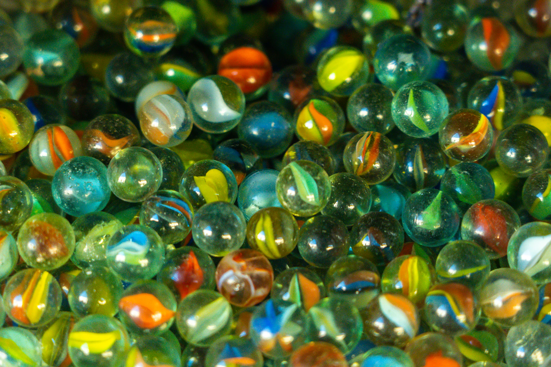 A heap of glass marbles seen close up, most of them clear with ribbons of orange, yellow, green and blue inside