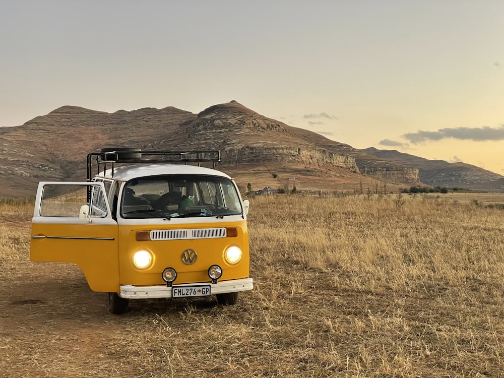 a yellow van parked in a field with mountains in the background
