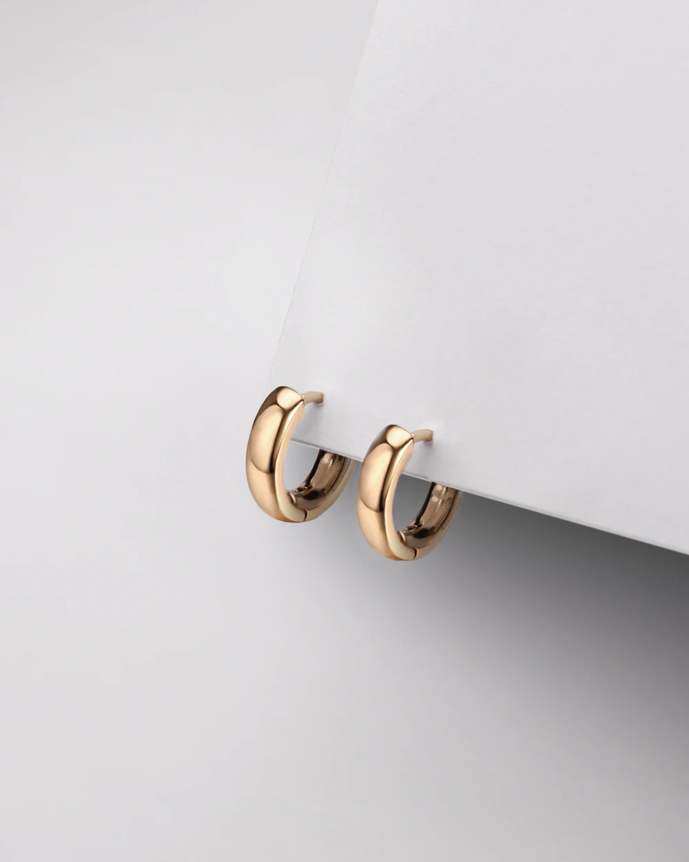 Pair of chunky gold hoop earrings on a paper backdrop