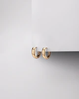 Minimalist gold hoop earrings displayed against a soft beige fabric background