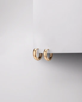 Minimalist gold hoop earrings displayed against a soft beige fabric background