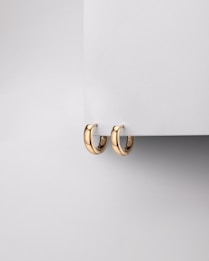 Two gold hoop earrings are elegantly displayed against a minimalist gray background, partially hanging from a flat surface.