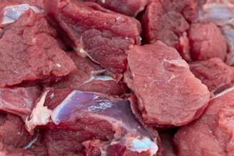 Raw pieces of red meat with visible marbling and texture are closely placed together, displaying pink and red hues with some surface moisture.