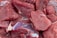 Raw pieces of red meat with visible marbling and texture are closely placed together, displaying pink and red hues with some surface moisture.