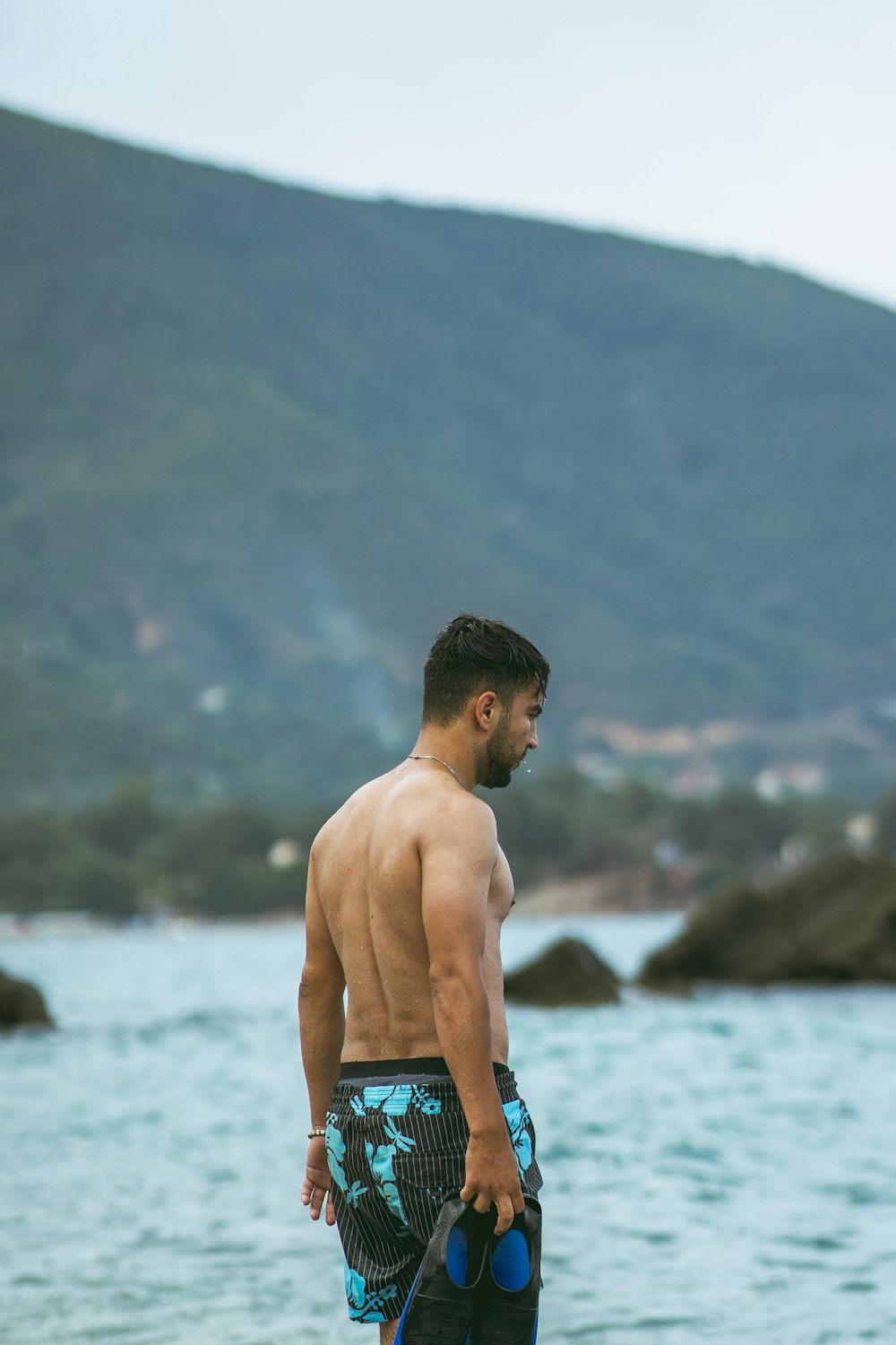 a shirtless man standing on a beach next to a body of water