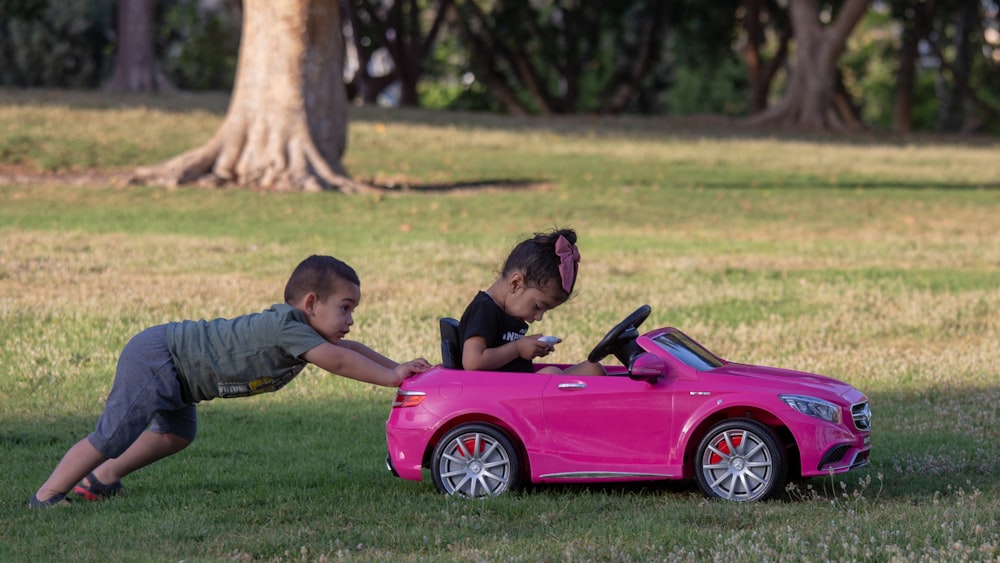 duas crianças que brincam com um carro de brinquedo cor-de-rosa