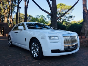 a white rolls royce parked in front of some trees